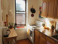 a kitchen with wooden cabinets and white appliances in front of a window that has potted plants on the counter