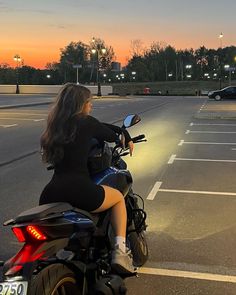 a woman riding on the back of a motorcycle down a street at sunset or dawn