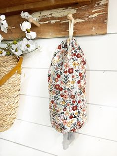 a bag hanging on the side of a wall next to flowers and baskets with handles