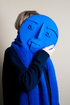 a woman holding up a blue mask with faces on it's face to her face