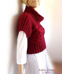 a mannequin wearing a red knitted sweater and white dress is leaning against a wall