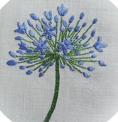 a blue flower is embroidered on a white linen circle with green stems in the center