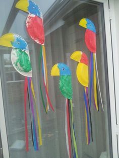 three colorful paper birds hanging from a window sill with streamers in the shape of parrots