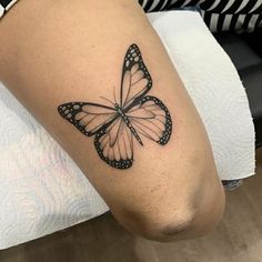 a black and white butterfly tattoo on the right leg, it is sitting on a woman's knee