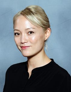 a woman with blonde hair wearing a black shirt and posing for a photo in front of a blue background