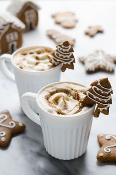 two white mugs filled with hot chocolate and decorated gingerbread cookies next to each other