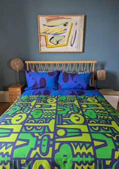 a bed with blue and green bedspread in a bedroom next to a painting on the wall