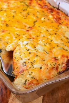 a cheesy casserole dish with a spoon in it on a wooden table