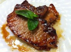 a piece of meat on a white plate with sauce and green leaf garnish