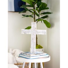 a wooden cross sitting on top of a white table next to a potted plant