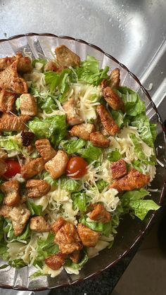 a salad with lettuce, tomatoes and chicken in a glass bowl on a counter