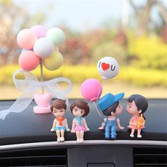 three small figurines sitting on the dashboard of a car with balloons in the air