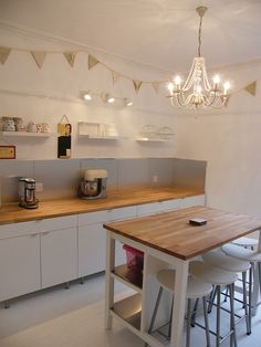 a kitchen with white cabinets and wooden counter tops next to a chandelier hanging from the ceiling