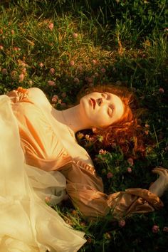 a woman laying in the grass with her head on her hands and eyes closed, wearing a white dress