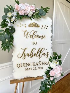 a welcome sign with flowers and greenery on it in front of a white wall