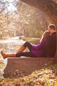 a man and woman sitting on a bench under a tree