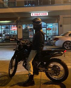 a man is standing next to his motorcycle on the street at night, in front of a liquor store