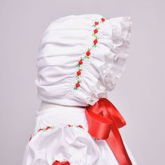 Complete your baby girl’s Christmas heirloom look with our sweet hand smocked bonnet! A Manolitas masterpiece, made from white batiste cotton fabric, trimmed with ecru vintage English lace and sweetly decorated with our signature Christmas Dulce hand smocked design. Its striking beauty lies in its gorgeous dainty hand smocking where bullion flowers in tones of bright red and green leaves travel in a wavy pattern creating perfect blend against its delicate white diamond hand smocking. White Bonnet, Hand Smocking, Striking Beauty, Wavy Pattern, Hand Smock, Sweet Christmas, Fall Holidays, Red Silk, Satin Ribbon