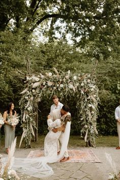 a bride and groom kissing in front of an outdoor wedding ceremony arch with greenery