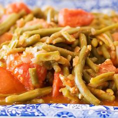 a blue and white plate topped with green beans, tomatoes and tomatoes covered in gravy