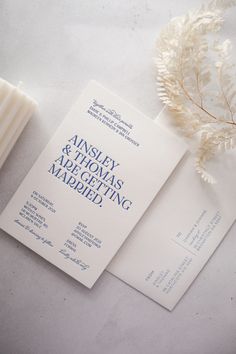 the wedding stationery is laid out next to a candle and some white flowers on a table