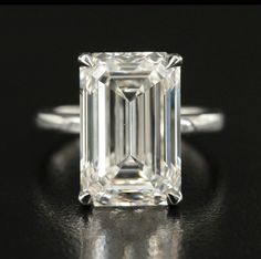 an emerald - cut diamond ring on a black surface, with the center stone in white gold