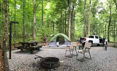 a truck parked in the woods next to a tent and picnic table with chairs around it