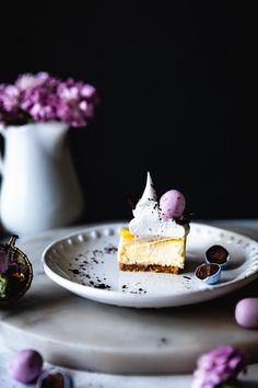 a piece of cheesecake on a plate next to some purple and white flowers in a vase