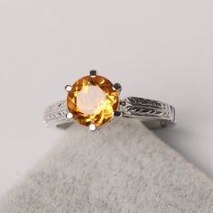 a ring with an orange stone in the center on a white cloth napkin, next to a