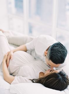 a man and woman laying in bed kissing