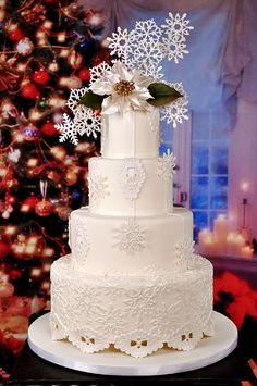 a white wedding cake with snowflakes and flowers on the top is sitting in front of a christmas tree