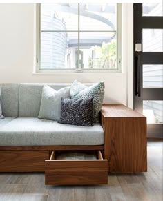 a couch with some pillows on it in front of a window and a wooden table