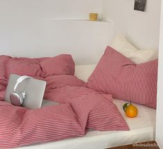 a laptop computer sitting on top of a bed covered in red and white striped sheets