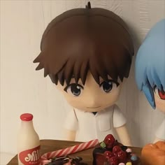 two anime figurines sitting on top of a table next to doughnuts