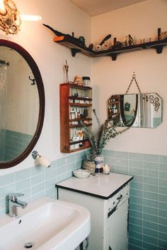 a bathroom with blue tiles and shelves above the sink is pictured in this image, there are two mirrors on the wall