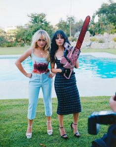 two women standing next to each other with a chainsaw on their shoulder and one holding a camera