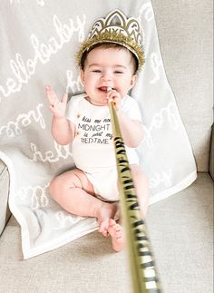 a baby sitting on a couch with a toothbrush in it's mouth and wearing a crown