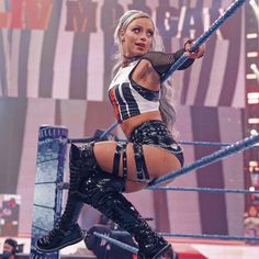 a woman in black and white outfit standing on top of a wrestling ring holding a rope