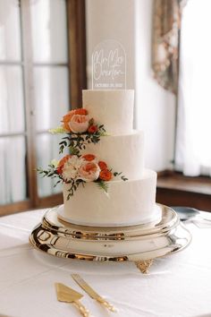 a white wedding cake with orange flowers on the top is sitting on a gold platter