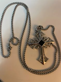 a silver cross on a chain with a black stone in the center is laying on a white surface