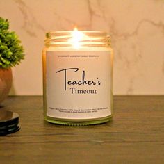 a lit candle sitting on top of a wooden table next to a potted plant