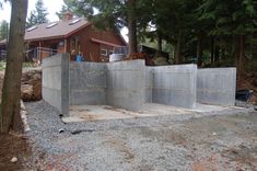 an unfinished concrete wall in front of a house with trees and rocks around it,