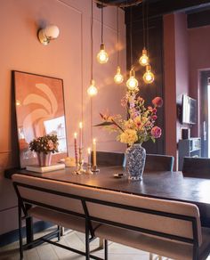 a vase with flowers and candles on a table in front of a painting hanging from the ceiling