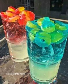 two glasses filled with different colored liquids on top of a glass table next to each other