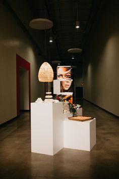 two white pedestals with flowers and cakes on them in an empty room next to hanging lights