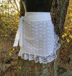 a mannequin wearing a white lace skirt on top of a tree in the woods