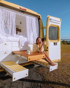 a woman sitting in the back of a yellow camper van eating food and drinking