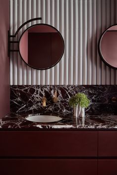 a bathroom with marble counter tops and two round mirrors on the wall above it, along with a vase filled with flowers