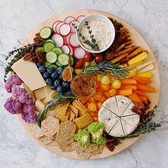 a platter filled with cheese, crackers, fruits and vegetables on a marble table