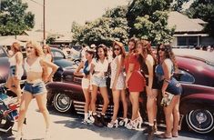 a group of young women standing next to each other in front of parked cars